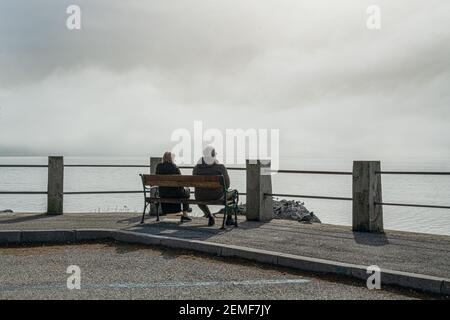 Trieste, Italia. 24 febbraio 2921. Un paio di anziani seduti su una panchina di fronte al mare Foto Stock