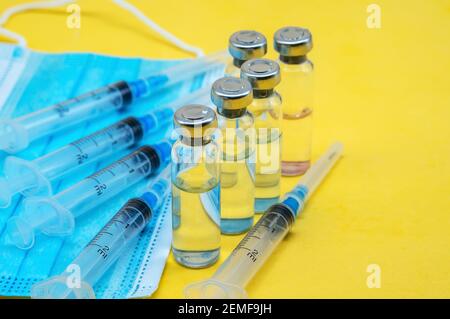 Prevenzione delle malattie stagionali. Fiale mediche, siringhe e una maschera su sfondo giallo. Vaccinazione contro covid-19. Foto Stock