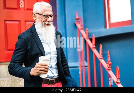 Uomo d'affari Hipster che cammina con una tazza di caffè da asporto Sfondo - la vecchia persona alla moda indossando abiti di moda casual - Felice stile di vita anziano Foto Stock