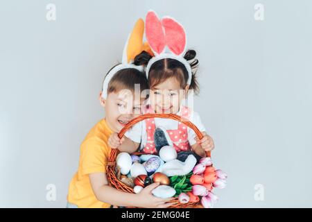 Un ragazzo e una ragazza vestita come un coniglietto che tiene un grande cesto con uova di Pasqua e tulipani. Preparazione per una vacanza in famiglia. Foto Stock