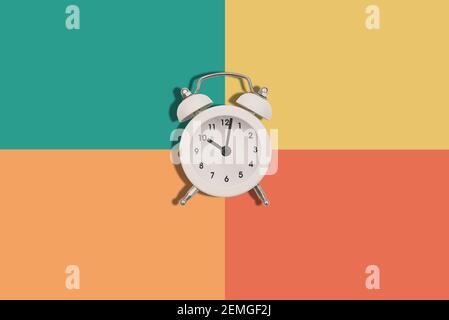 Sveglia su sfondo colorato. Le mani dell'orologio mostrano le dieci di sera o di mattina. Stile minimale alla moda. Disposizione piatta. Foto Stock