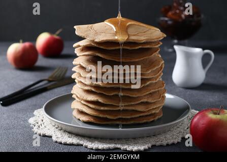 Frittelle dolci fatte in casa con mele versate con sciroppo dolce su sfondo grigio Foto Stock