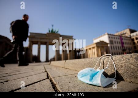 25 febbraio 2021, Berlino: Una guardia dal naso a bocca si trova a terra di fronte a Brandenburger, mentre un passerby cammina. Foto: Christoph Soeder/dpa Foto Stock
