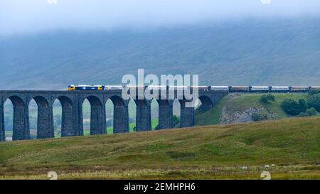 Locomotiva per trasporto diesel (treno ferroviario GB) e carri tarmac che attraversano il viadotto panoramico Ribblehead di Misty Foggy Whernside - Yorkshire Dales, Regno Unito Foto Stock