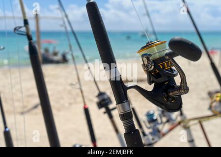 Canna da pesca in primo piano e mulinello di fronte al mare, sullo sfondo l'Oceano dei Caraibi e le barche ormeggiate in una spiaggia messicana Foto Stock