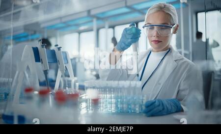 Medical Research Laboratory: Ritratto di una bella scienziata femminile in occhiali di protezione utilizzando micropipetta per analisi di prova. Advanced Scientific Lab per Foto Stock