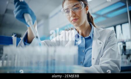 Medical Research Laboratory: Ritratto di una bella scienziata femminile in occhiali di protezione utilizzando micropipetta per analisi di prova. Advanced Scientific Lab per Foto Stock