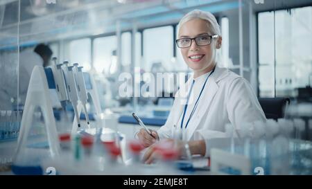 Laboratorio di Ricerca medica: Ritratto di una bella scienziata femminile che scrive i dati, sorridendo sulla macchina fotografica. Advanced Scientific Lab for Medicine Foto Stock