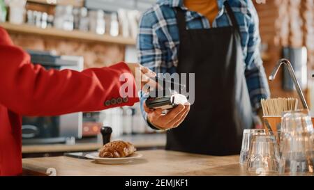 Primo piano di una mano femminile tenere uno smartphone con una tecnologia di pagamento NFC utilizzata per pagare per croissant in un caffè. Il cliente utilizza il cellulare per pagare Foto Stock