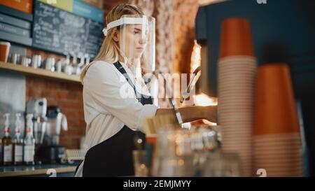 Bella giovane barista indossare Face Shield sta facendo una tazza di caffè fresco in un caffè. Bar dipendente che lavora nel Coffee Shop Restaurant. Sociale Foto Stock