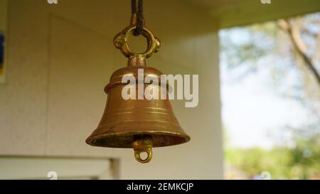 Nuova campana di bronzo nel tempio indiano isolato su sfondo sfocato. Primo piano della campana di ottone del tempio indù appesa in color oro Foto Stock