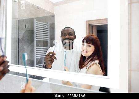 In bagno. Riflessione nello specchio della coppia multirazziale positiva, la bana nera e la bella donna europea, spazzolando i denti insieme Foto Stock