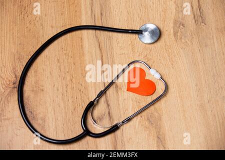 Stetoscopio con cuore rosso all'interno, su sfondo ligneo. Simbolo della salute e della medicina. Heartbeat per volantini, poster, web, banner e schede Foto Stock