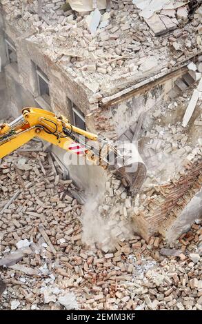 Demolizione di vecchi edifici in mattoni con benna per escavatore in nube di polvere, vista dall'alto. Foto Stock