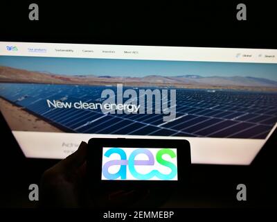 Persona che detiene smartphone con il logo della società elettrica statunitense AES Corporation sullo schermo di fronte al sito Web. Mettere a fuoco il display del telefono. Foto Stock