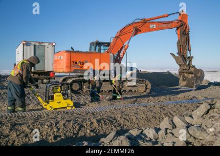 Lavoratori maschi e escavatori che installano culvert durante la costruzione invernale della Inuvik-Tuktoyaktuk Highway, l'Artico del Canada. Foto Stock