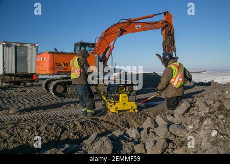 Lavoratori maschi e escavatori che installano culvert durante la costruzione invernale della Inuvik-Tuktoyaktuk Highway, l'Artico del Canada. Foto Stock