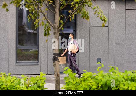 Giovane uomo di consegna in maschera medica sul viso tenendo in mano i sacchetti di carta. Corriere uomo Hipster con borse per la spesa. Servizio di consegna online sicuro Foto Stock