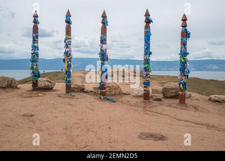 Una serie di serge a Shamanka sull'isola di Olkhon. Fila di alte colonne religiose rituali Buryat legate con nastri colorati, sullo sfondo blu di sk Foto Stock