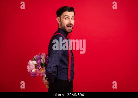 Profilo lato foto di giovane buon umore eccitato gentiluomo stupito nascondi bouquet sorpresa isolato su sfondo rosso Foto Stock