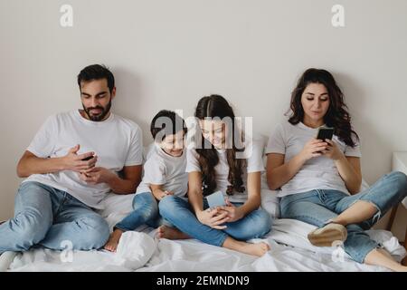 Famiglia a letto con smartphone. Concetto basato sulla tecnologia digitale. Foto Stock