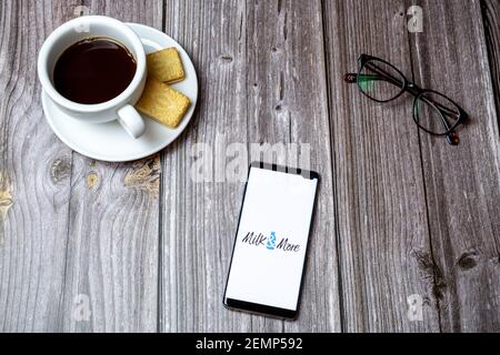 Un telefono cellulare o cellulare su un tavolo di legno Con l'app latte e altro ancora aperta accanto a caffè e bicchieri Foto Stock