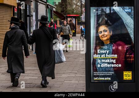 Londra, Regno Unito. 25 Feb 2021. La gente passa i cartelli informativi del Covid del governo mentre si prepara per Purim in Stamford Hill, una delle zone con la più alta incidenza di infezioni di Covid 19 a Londra. Purim è un festival ebraico di 24 ore, che celebra la sopravvivenza degli ebrei minacciati di estinzione in Persia. Comprano i regali di cibo di Mishloach Manos alla famiglia e agli amici. National Lockdown 3 con l'istruzione del governo per tutti di rimanere a casa per salvare la pressione sul NHS. Credit: Guy Bell/Alamy Live News Foto Stock