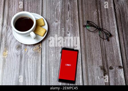 Un telefono cellulare o cellulare su un tavolo di legno Con l'app LNER aperta accanto a un caffè e. occhiali Foto Stock