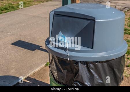 Una maschera chirurgica per il viso indossata per il coronavirus che si attacca a metà di una spazzatura può coprire in un parco pubblico scartato mettendo incautamente danno ad altri Foto Stock