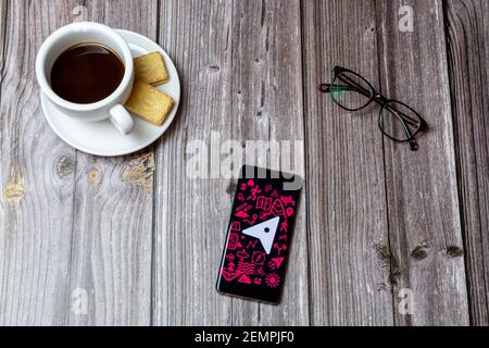 Un telefono cellulare o cellulare su un tavolo di legno Con l'app OS Maps aperta accanto a un caffè e bicchieri Foto Stock