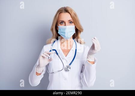 Foto di una siringa per la tenuta a mano da donna professionale che indossa la sicurezza a freddo maschera medica isolata su sfondo grigio Foto Stock