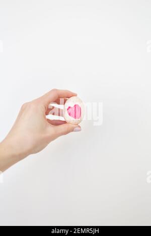 Una ragazza che tiene un uovo di Pasqua con un cuore rosa dipinto con acquerelli in mano, isolato su uno sfondo bianco Foto Stock