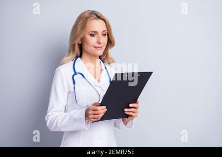 Foto di bella donna medica matura che legge informazioni in elenco di controllo isolato su sfondo grigio Foto Stock