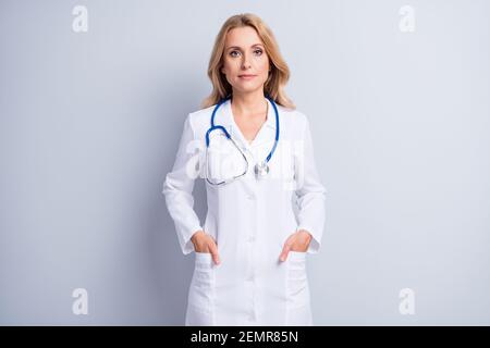 Foto di affascinante persona messo le mani in tasche stetoscopio appendere sul collo isolato su sfondo grigio Foto Stock