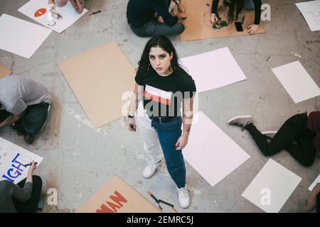 Ritratto di donna in piedi mentre si preparano attivisti maschili e femminili cartelli nell'edificio Foto Stock