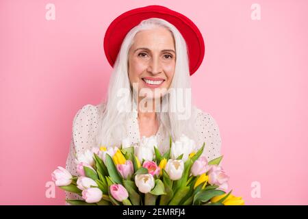 Ritratto di attraente allegro grigio-capelli granaio che tiene tulipani romanticismo evento negozio di floristry isolato su sfondo di colore rosa pastello Foto Stock