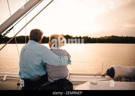 Vista posteriore della coppia senior che si affaccia sul mare durante il tramonto Foto Stock