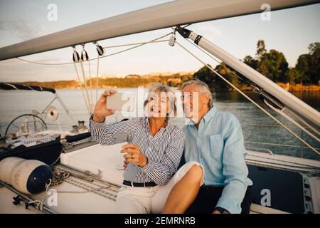 Sorridente coppia senior che prende selfie sullo smartphone mentre si è seduti in barca Foto Stock