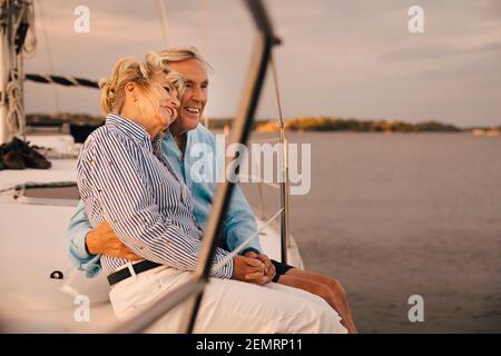 Felice coppia senior seduta sul bordo della barca a vela durante il tramonto Foto Stock