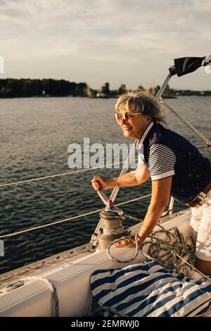 Donna anziana sorridente che gira manico sulla barca in mare durante giorno di sole Foto Stock