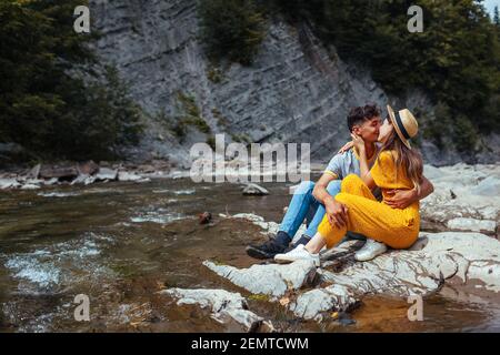Coppia di turisti che si baciano dal fiume di montagna godendo di paesaggio. I viaggiatori si agguonano seduti sulla roccia. Vacanza estiva viaggio. Vista posteriore Foto Stock