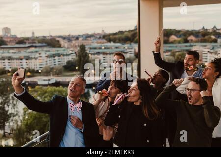 Allegri colleghi di sesso maschile e femminile che prendono selfie su smartphone durante la festa in ufficio Foto Stock