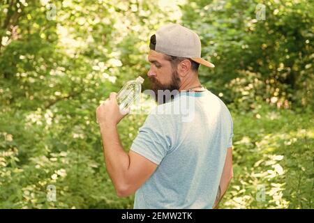 Ogni SIP conta. Ragazzo maturo in cappello. Viaggiatore hipster assetato. Acqua potabile nella foresta all'aperto con tramonto natura sullo sfondo. Uomo bearded con bottiglia d'acqua. Ritratto di fitness dell'uomo bearded. Foto Stock