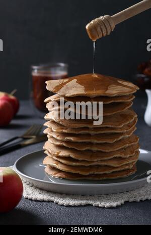 Frittelle dolci fatte in casa con mele versate sopra con sciroppo dolce su uno sfondo grigio scuro. Formato verticale Foto Stock