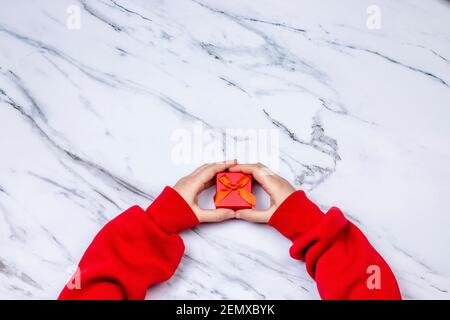 Le mani della ragazza che reggono regalo o scatola di regalo con nastro su sfondo di marmo bianco piatto posa top wave. Regalo per compleanno, San Valentino, Natale, nuovo Foto Stock