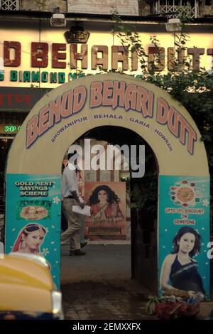 Un uomo che cammina sulla passerella di una zona d'affari, visto attraverso una porta a lato della strada decorata con pubblicità a Kolkata, Bengala Occidentale, India. Foto Stock