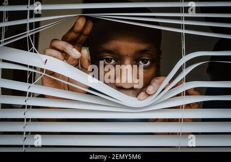 Uomo depresso che guarda fuori dalle tende della finestra a casa Foto Stock