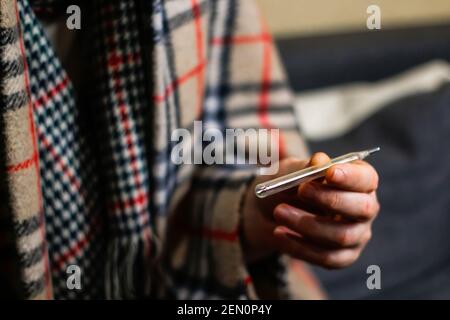 VV, Ucraina - 21.11.2020: Defocus Guy misura la temperatura. Immagine senza volto dell'uomo malato freddo a casa in plaid a scacchi caldi, presa della mano dell'uomo Foto Stock