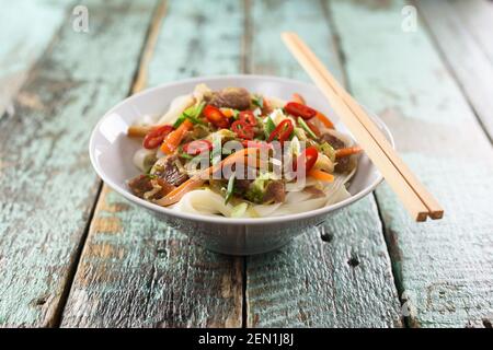 Noodle tradizionali asiatiche. Udon mescolare i tagliatelle con carne, verdure e peperoncino in una ciotola con i bastoncini di pollo su rustico sfondo di legno con copyspace Foto Stock