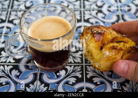 Tenere a mano una crostata portoghese chiamata Pastel de nata, con caffè espresso nero Foto Stock